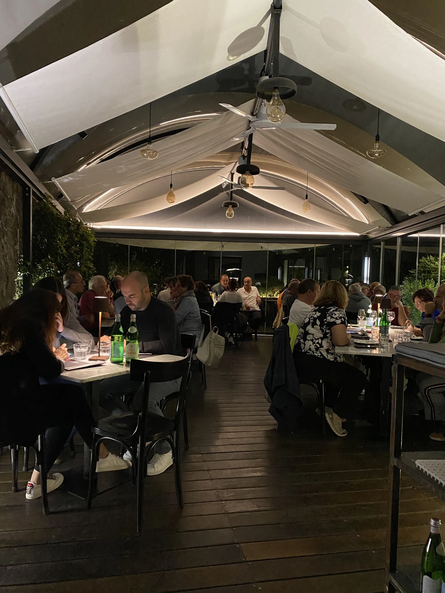 Veranda coperta a vele con ospiti a cena illuminata da luce perimetrale indiretta e sospensioni calde a Pepe in Grani
